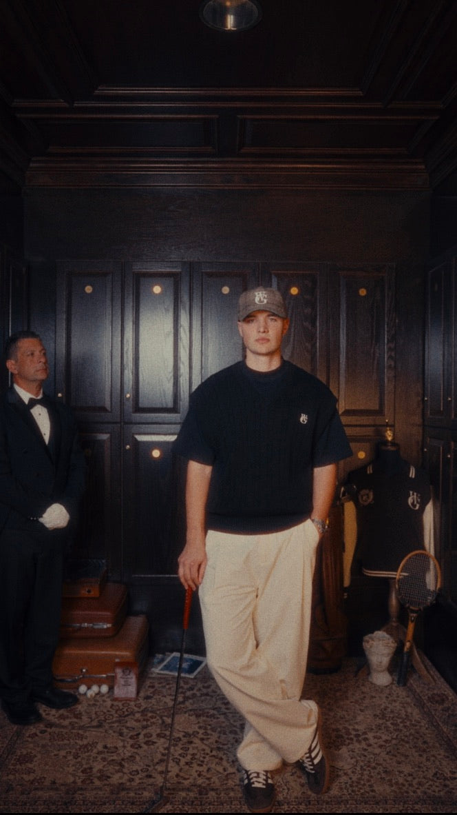 A member in the Woodgrain clubhouse locker room, wearing the cable knit sweater vest and pleated trouser